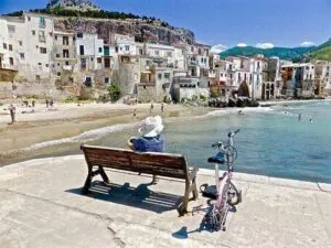 Persona seduta su una panchina davanti alle case sul mare di Cefalù